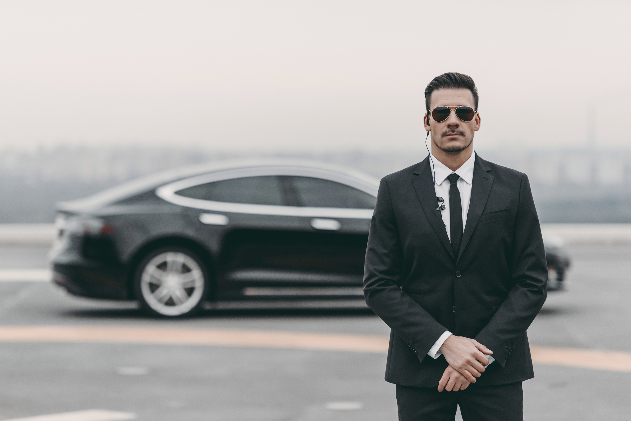 serious bodyguard standing with sunglasses and security earpiece on helipad | Close Protection Agency London