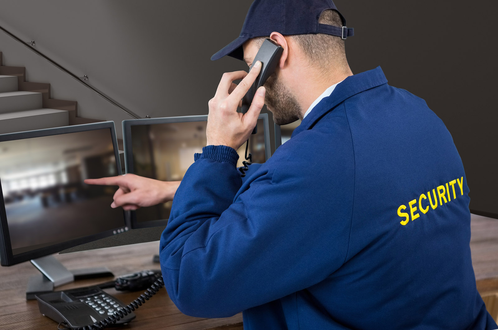 Security guard in his office phoning and pointing something in the screen | Security Monitoring London